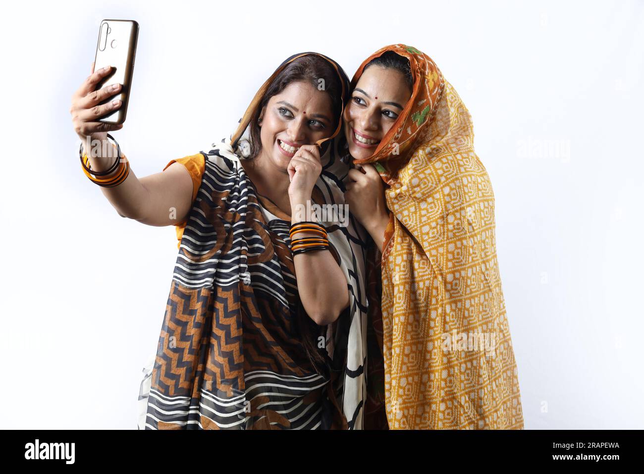 Ländliche indische glückliche Frauen in Saree, die verschiedene Ausdrucksformen des Dorflebens darstellen. Sie halten ein Handy und machen ein Selfie Stockfoto