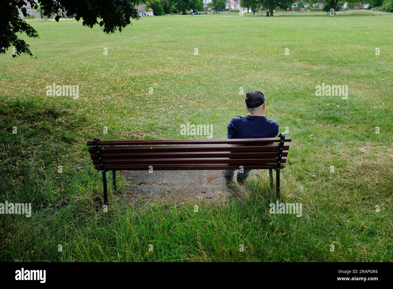 Ein alter Mann, der auf einer Parkbank sitzt. Stockfoto