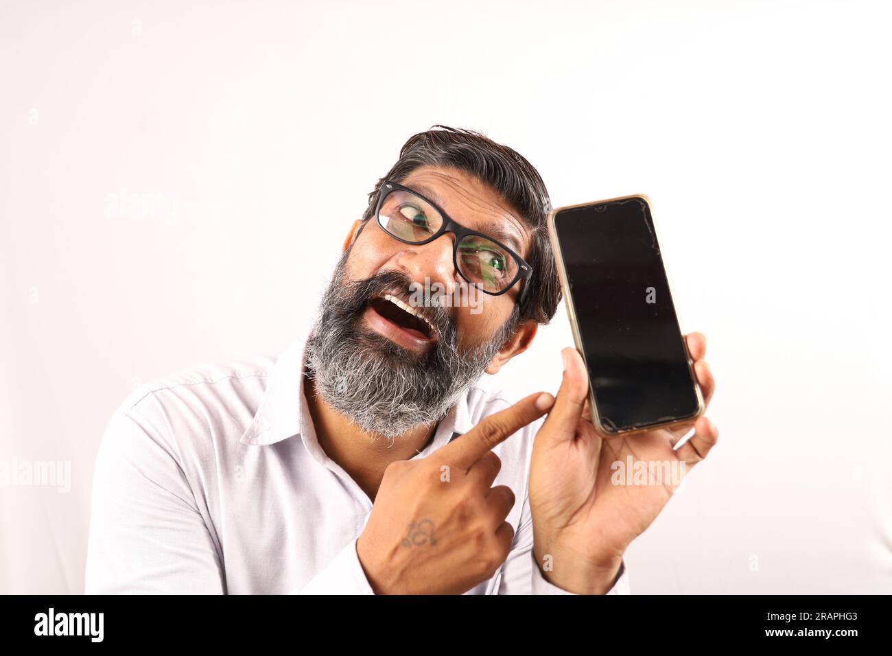 Mittelalter, bärtiger Indianer, der ein Hemd in der Hand hält und ein Handy in der Hand zeigt. Flippige Ausdrücke auf einem Ebenen Hintergrund. Stockfoto