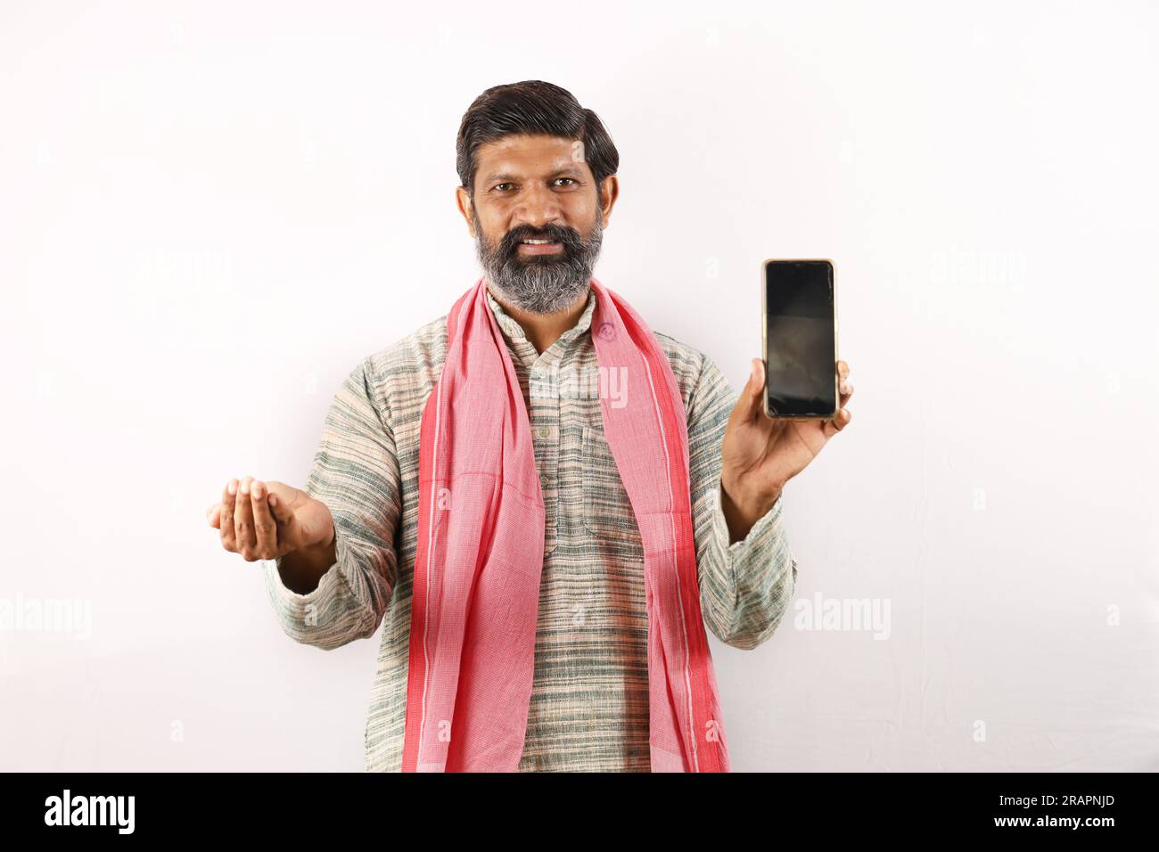 Fröhlicher Landwirt, der den Bildschirm des Mobiltelefons zeigt und Technologie verwendet. Samen in der anderen Hand. Glücklicher indischer bärtiger Bauer im ländlichen Indien Konzept. Stockfoto