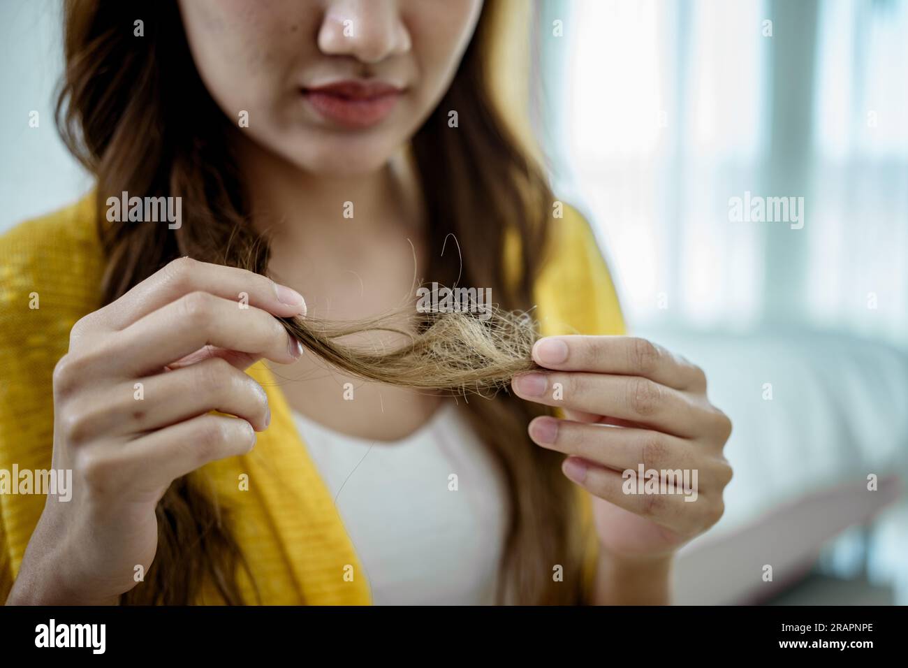 Eine junge Frau, die ihr entjungfertes Haar hält und ansieht. Stockfoto