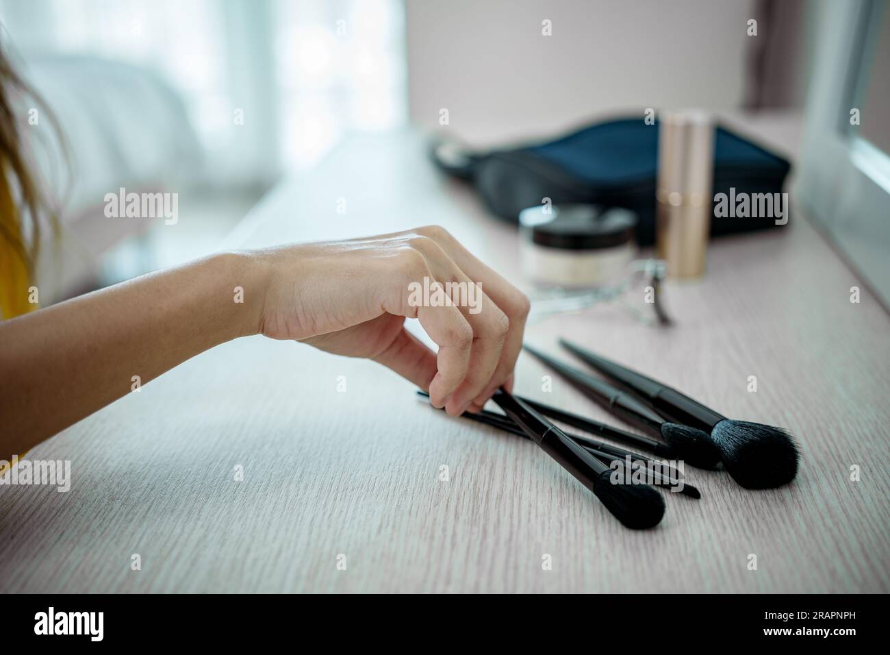 Eine Frau, die Make-up-Pinsel mit Kosmetikprodukten auf dem Tisch hält. Stockfoto