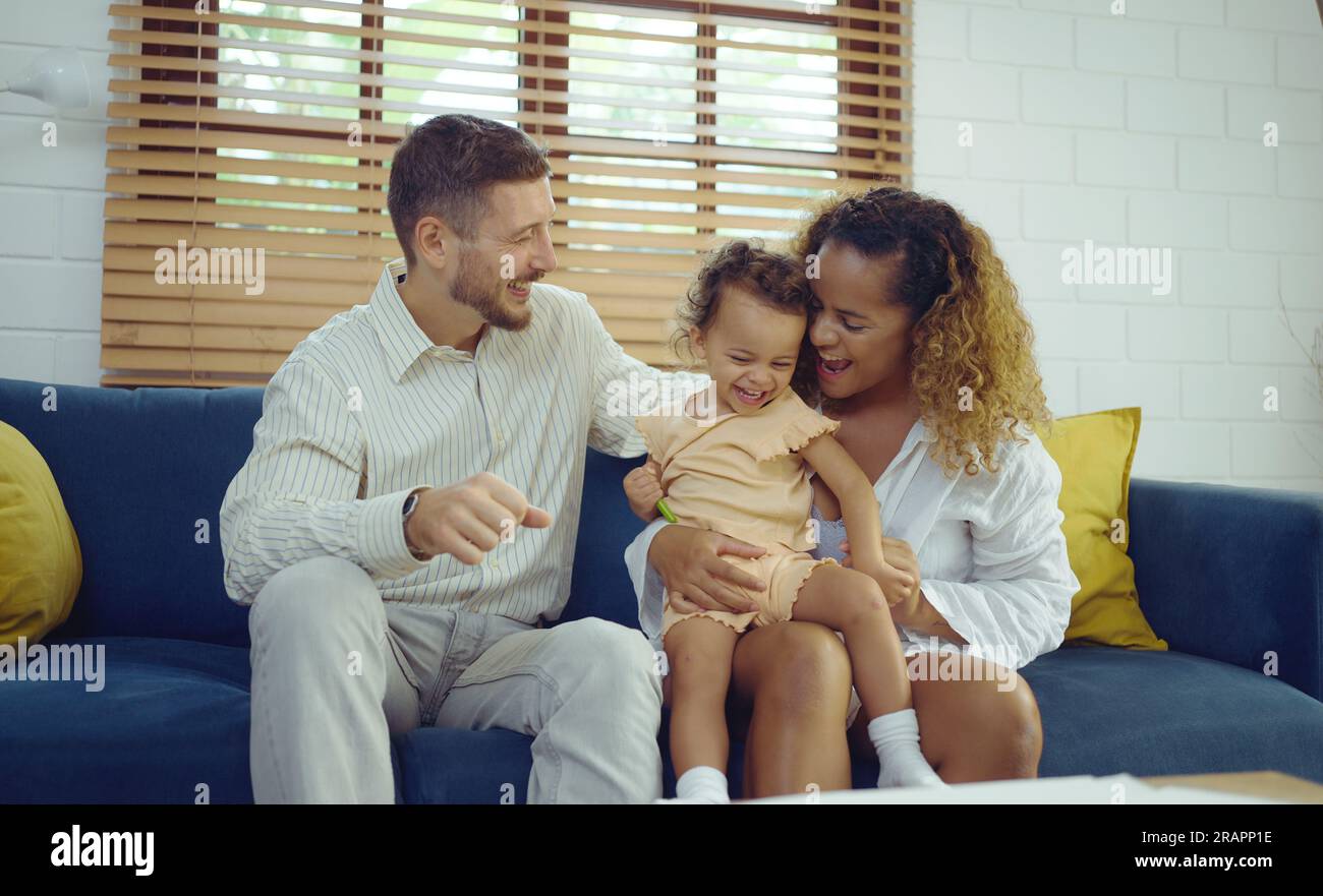 Fröhliche Eltern, die Spaß mit ihrer süßen Tochter haben und sich zusammen auf dem Sofa umarmen, um den Familienleben zu Hause zu genießen Konzept. Stockfoto
