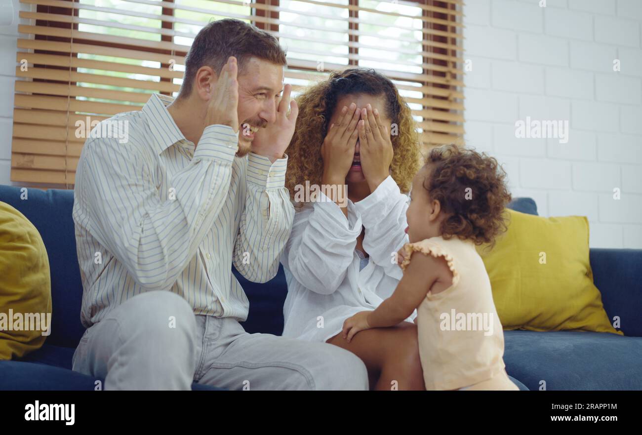 Fröhliche, fröhliche Eltern und süße Tochter spielen zusammen Guck-Guck auf dem Sofa. Stockfoto