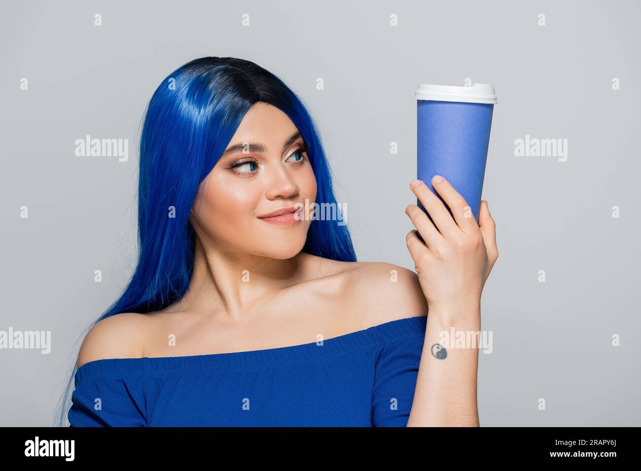 Zum Mitnehmen, junge Frau mit blauem Haar und Augen, die Kaffee auf grauem Hintergrund hält, Essen zum Mitnehmen, Koffein, Energie, Tattoo, Lebendige Farben, selbst ablaufend Stockfoto