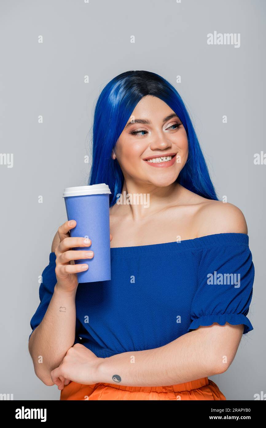 Positive Einstellung, Einwegbecher, junge Frau mit blauem Haar und Augen, die Kaffee auf grauem Hintergrund hält, Essen zum Mitnehmen, Koffein, Energie, Tattoo, VIBRANT c Stockfoto