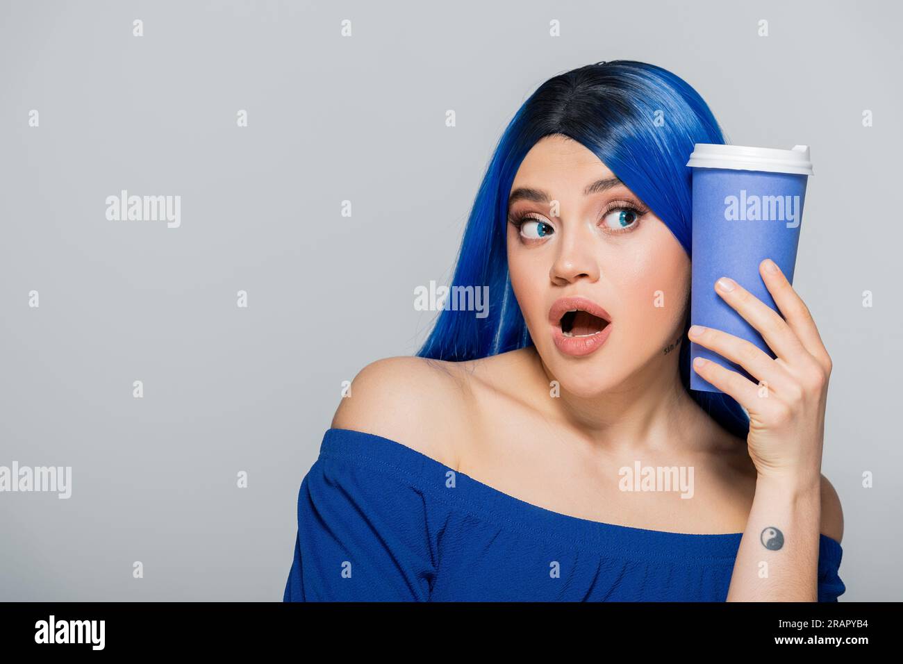 Zum Tassen, erstaunt, junge Frau mit blauem Haar und Augen, die Kaffee auf grauem Hintergrund hält, zum Mitnehmen, Koffein, Energie, Tattoo, Leuchtende Farben, Stockfoto