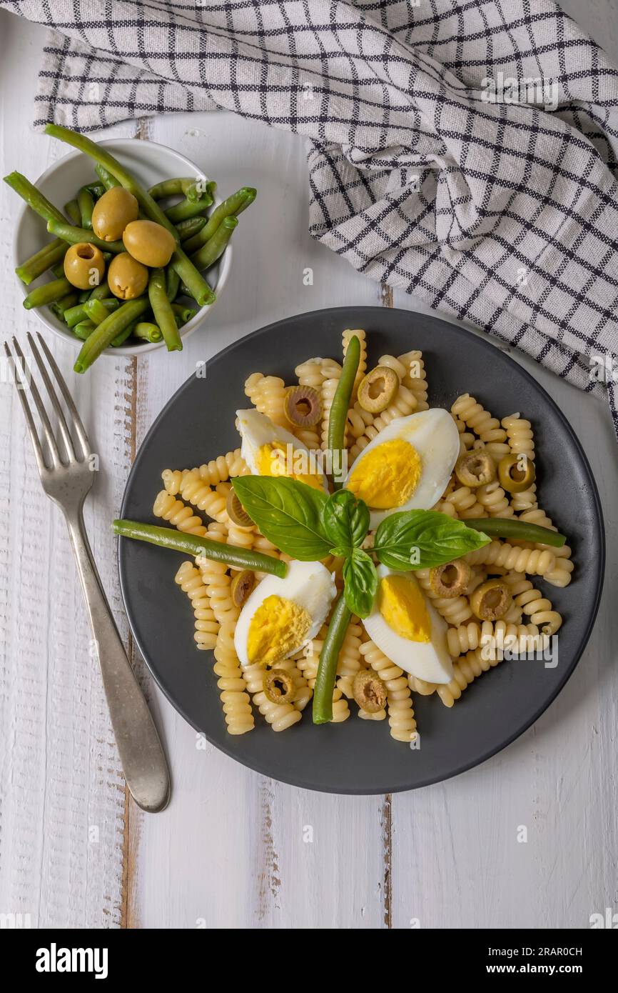 Ein Teller mit kalter Pasta mit gekochten Eiern, gekochten grünen Bohnen, Oliven und Basilikumblättern Stockfoto