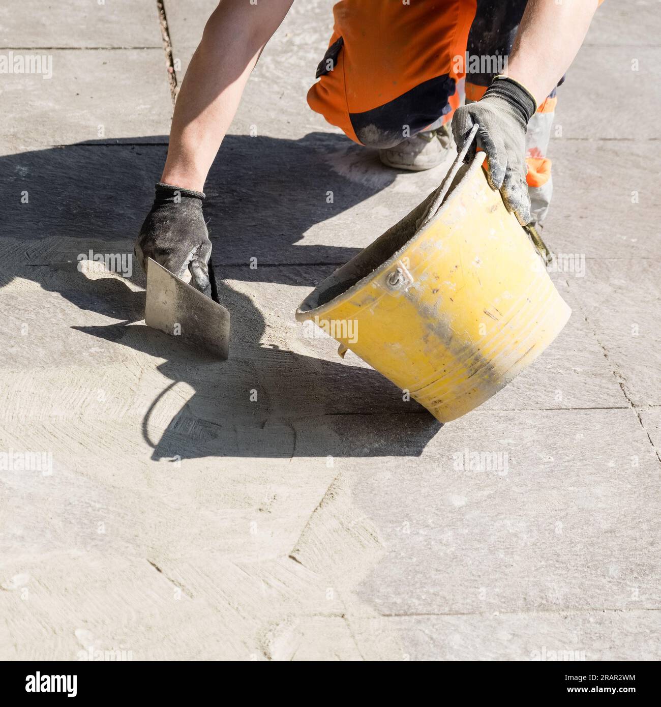 Echte Szene, Arbeiter mit Kelle und Eimer, der auf einem Fußgängerweg arbeitet. Stockfoto