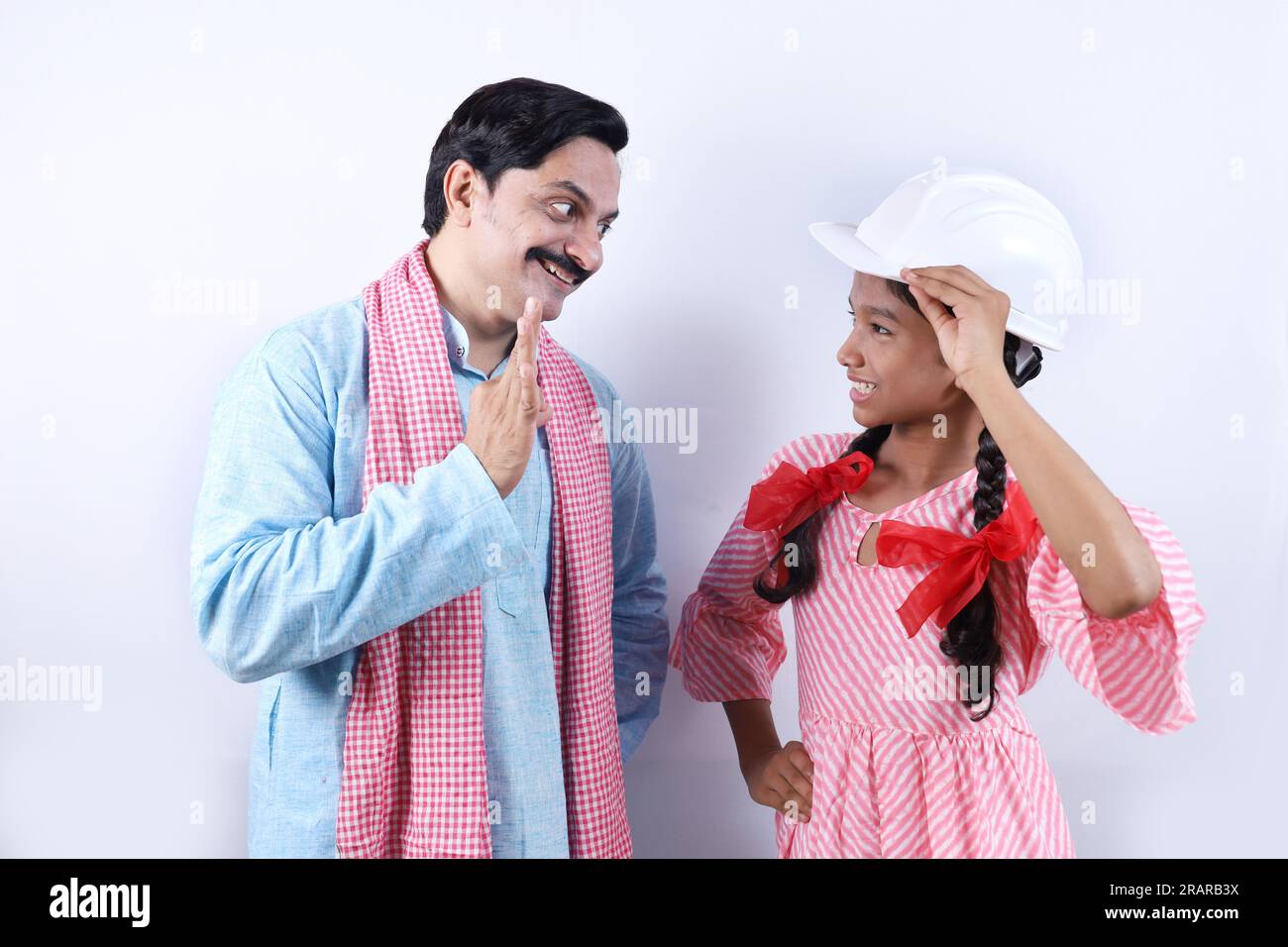 Der ländliche indische glückliche Dorfvater in Kurta Pyjama steht mit seiner selbstbewussten Tochter. Die Tochter trägt einen Helm und ist bereit für die strahlende Zukunft Stockfoto