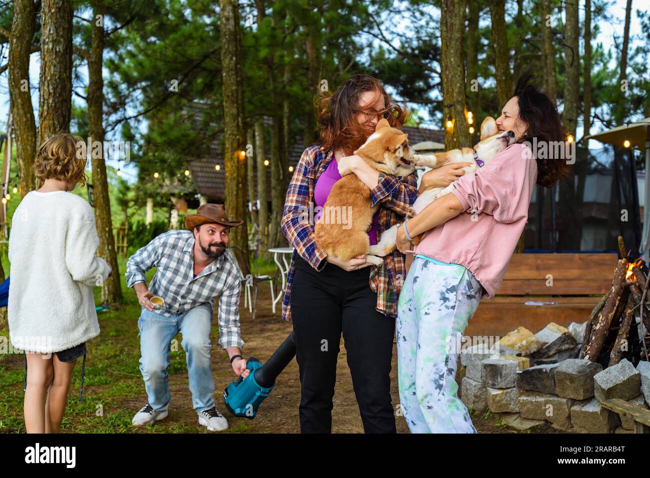 Lustiger Familienmoment mit dem Vater, der einen Gartenbläser benutzt, um seine Frau und seine Tochter zu ärgern, die Hunde halten Stockfoto