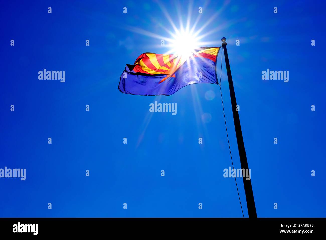 Die Staatsflagge von Arizona fliegt im Wind auf einem Fahnenmast mit Sonnenschein sunstar am blauen Himmel Stockfoto