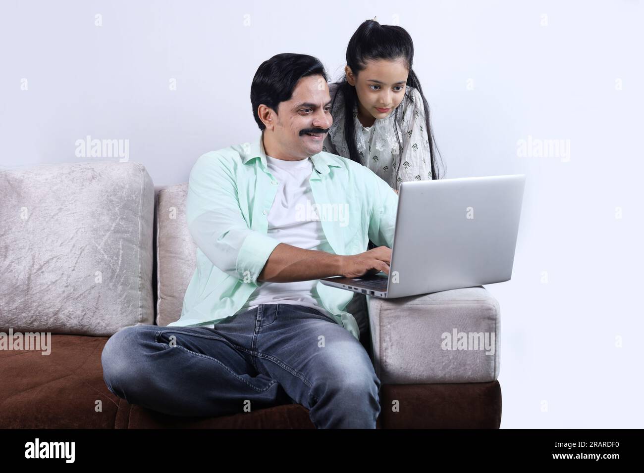 Glückliche indische Familie mit alleinerziehendem Vater und Tochter, die mit einem Laptop surfen und eine angenehme Zeit zusammen verbringen. Die Familie schaut sich das Notebook an. Stockfoto