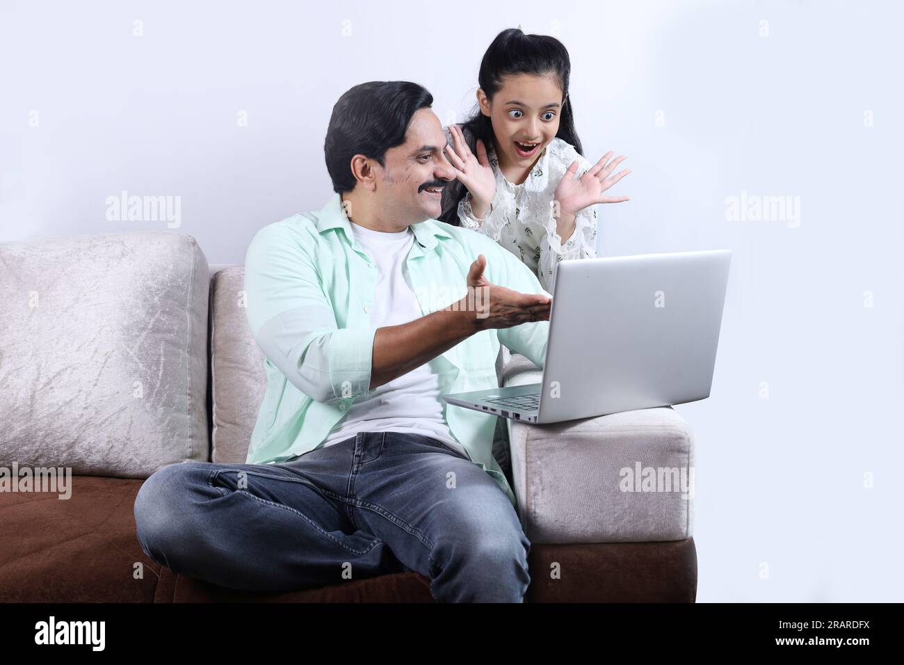 Glückliche indische Familie mit alleinerziehendem Vater und Tochter, die mit einem Laptop surfen und eine angenehme Zeit zusammen verbringen. Die Familie schaut sich das Notebook an. Stockfoto