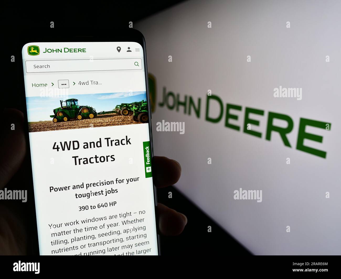 Person, die ein Mobiltelefon mit einer Webseite des US-amerikanischen Unternehmens Deere and Company (John Deere) auf dem Bildschirm vor dem Logo hält. Konzentrieren Sie sich auf die Mitte des Telefondisplays. Stockfoto