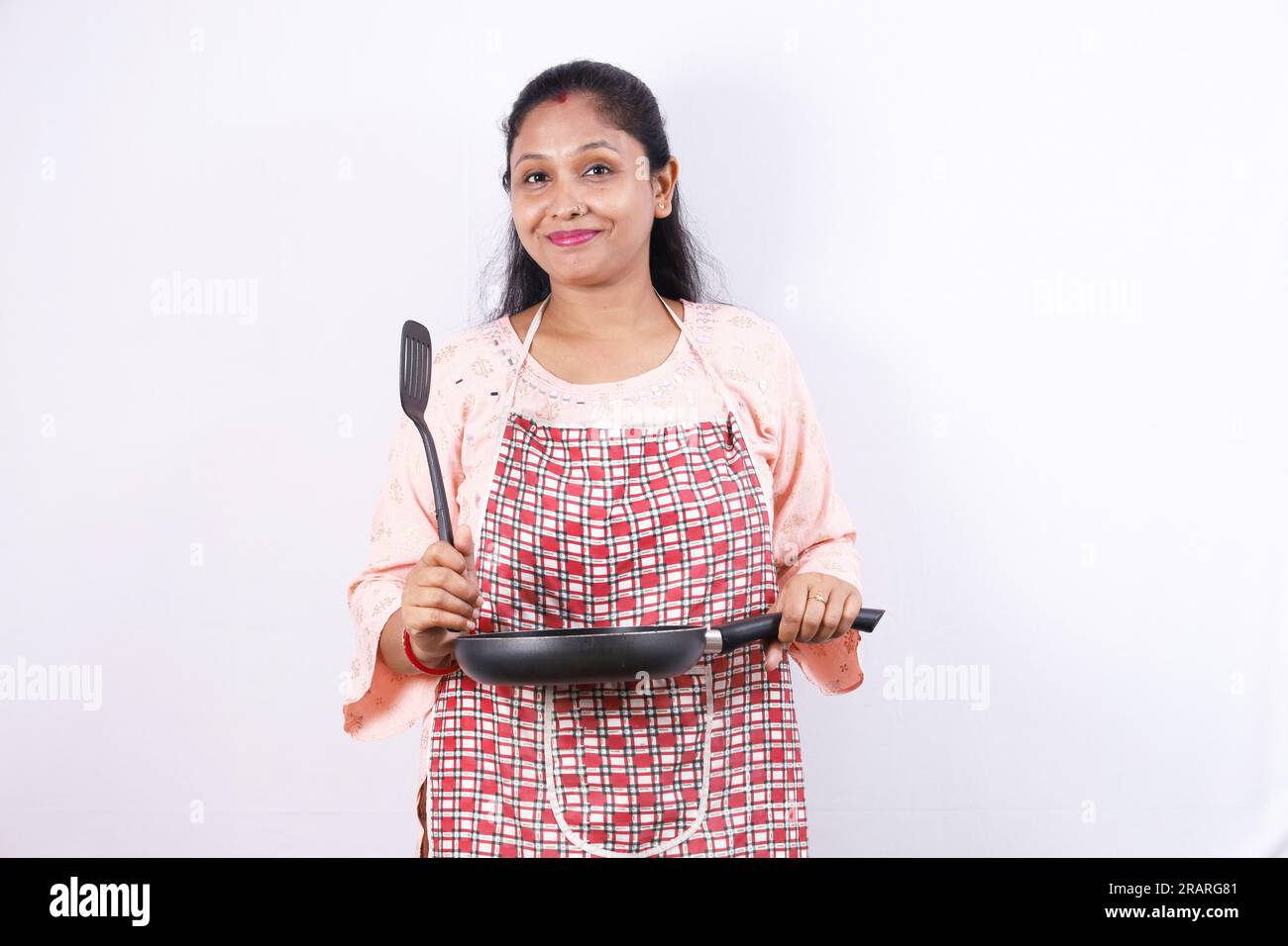 Glückliche indische Hausfrau, die einen Bratlöffel in der Hand hält und eine Kochmütze trägt, die verschiedene Stimmungen des Küchenchefs mit Schürze zeigt. Stockfoto