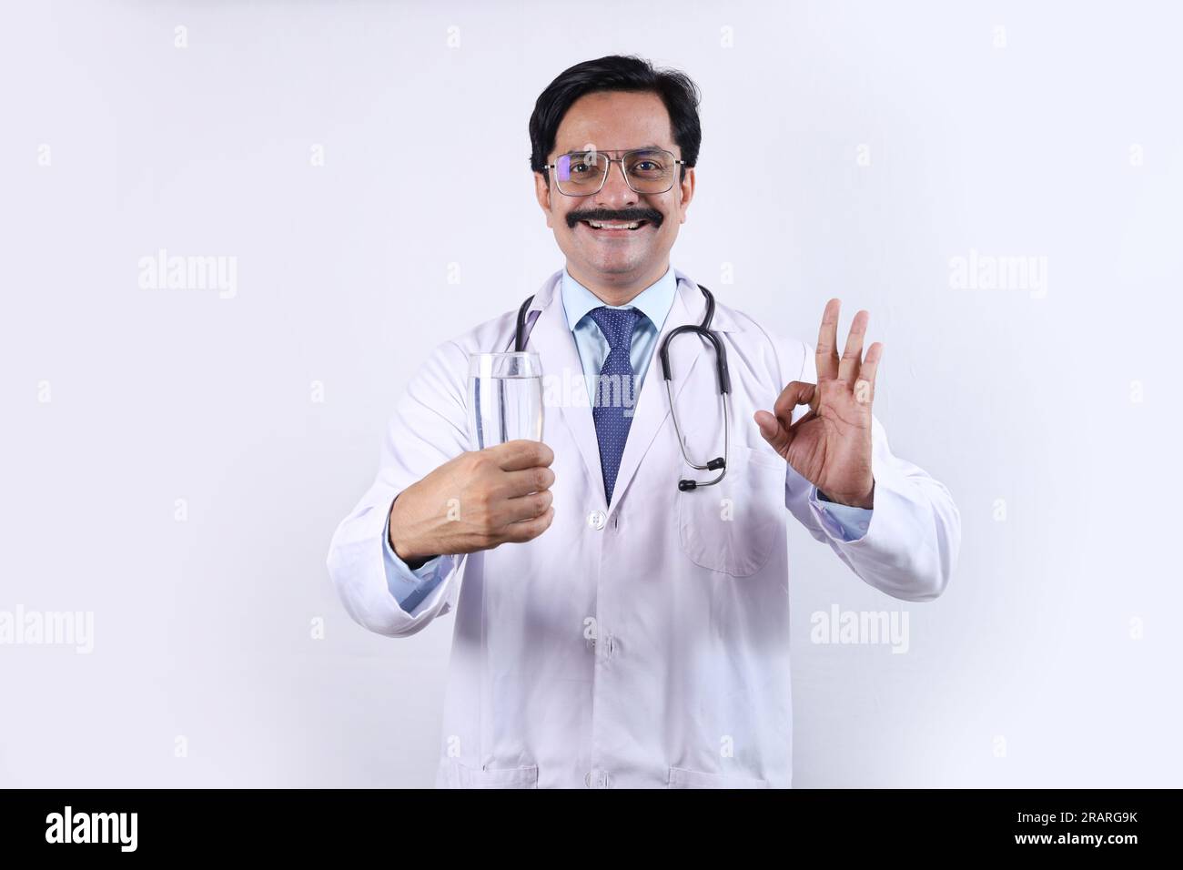 Indischer selbstbewusster Doktor hält ein Gesundheitsgetränk in der Hand und schlägt vor, frisch und gesund zu trinken. Der Arzt steht auf weißem Hintergrund. Stockfoto