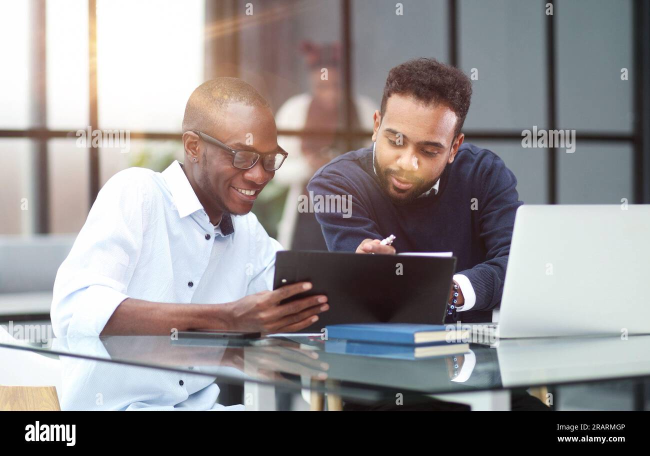 Kollegen, die an einem Tisch in einem modernen Büro sitzen und mit einem Laptop sprechen Stockfoto