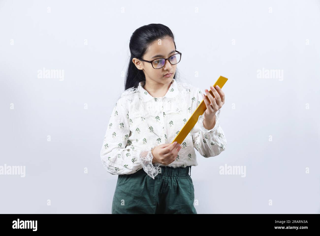 Junge Lehrerin. Porträt eines glücklichen indischen Teenagers, das eine Messskala in der Hand hält und eine Brille trägt. Monitorkonzept der jungen Klasse. Stockfoto