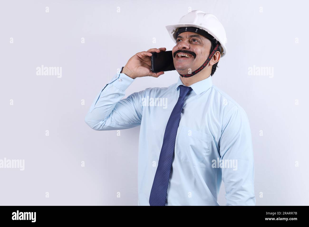 Glücklicher indischer Bauarbeiter, der Ingenieurkonzept für eine bessere Zukunft macht. Der fröhliche Ingenieur trägt einen technischen Helm. Telefonieren. Stockfoto