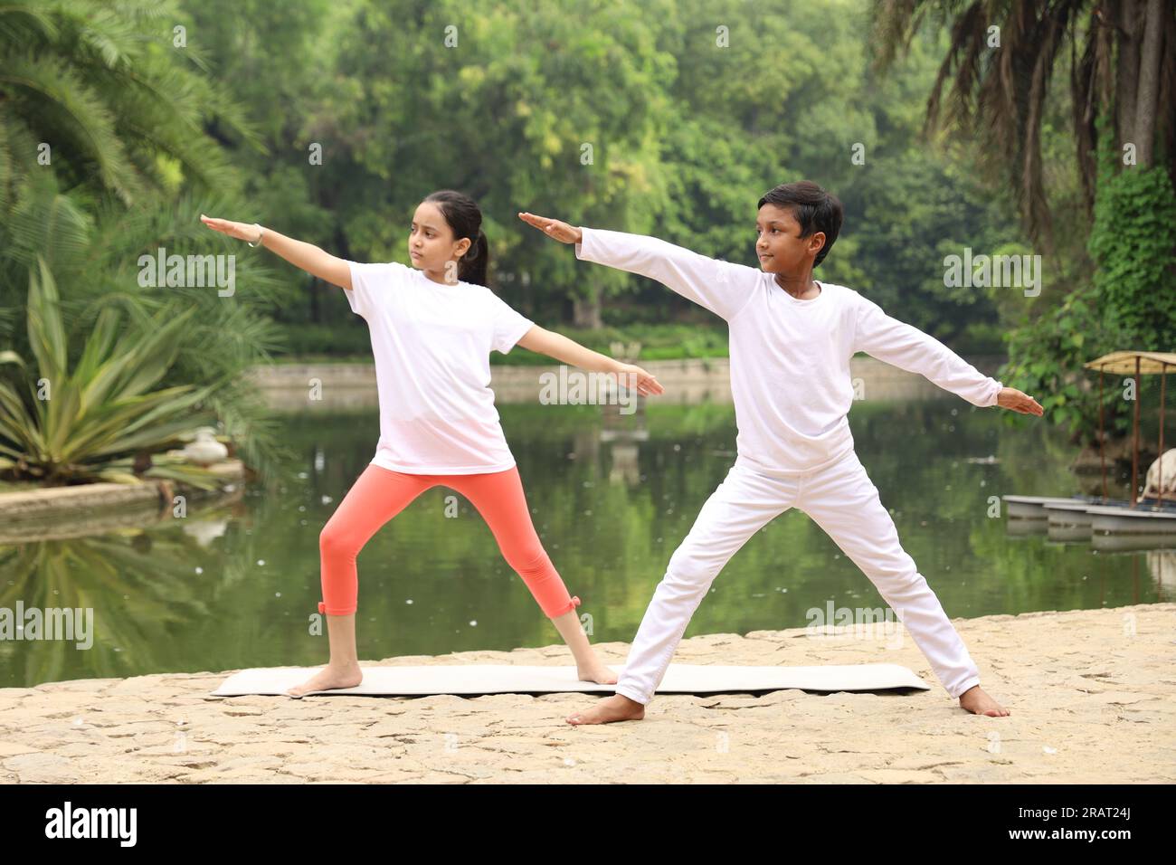 Junge Kinder, die früh am Morgen Yoga-Übungen in einem grünen öffentlichen Park machen. Wir können Wasserkörper sehen. Kinder sind gesundheitsbewusst. Internationaler Yoga-Tag. Stockfoto