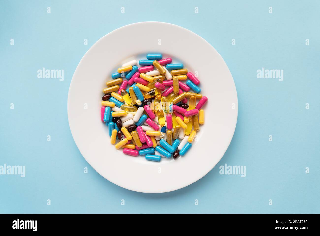 Bunte Pillen in einer großen weißen Schüssel auf blauem Hintergrund. Gesundheitsbegriff und evidenzbasierte Medizin. Platz für eine Inschrift Stockfoto
