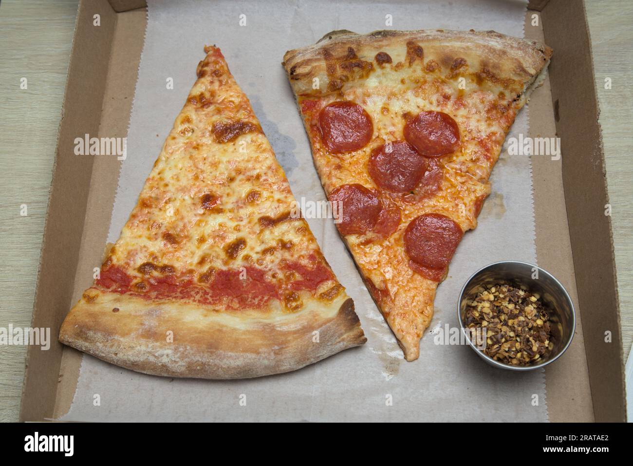 New yorker Pizzastück (Pepperoni, einfache Scheibe) nyc-Pizzeria mit zerdrückten roten Pfefferflocken auf fettigem Pergamentpapier, Pappschachtel Stockfoto
