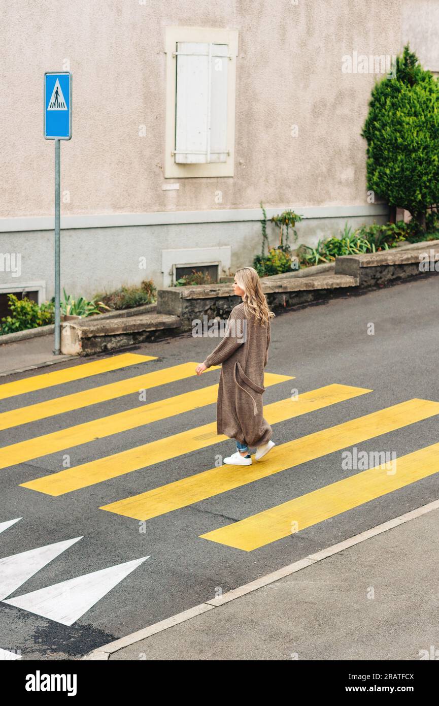 Modefrau, die den roadm überquert und eine lange Strickjacke trägt Stockfoto