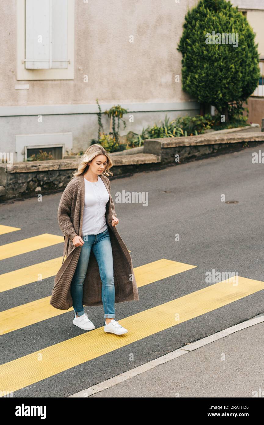 Modefrau, die den roadm überquert und eine lange Strickjacke trägt Stockfoto
