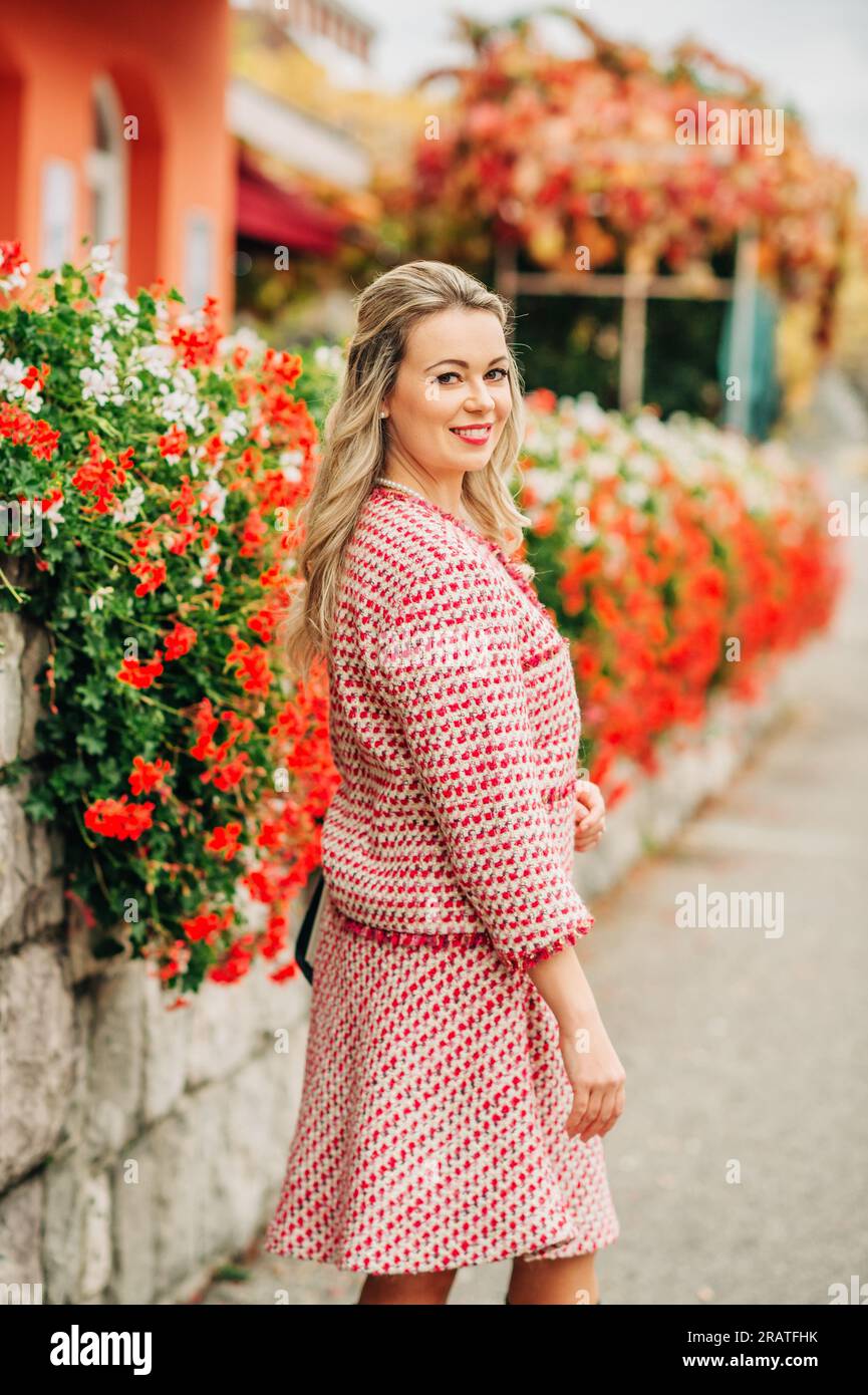 Retro-Porträt einer schönen Frau mit blonden Haaren, die auf einer Terrasse steht und einen rot-weiß karierten Blazer trägt Stockfoto