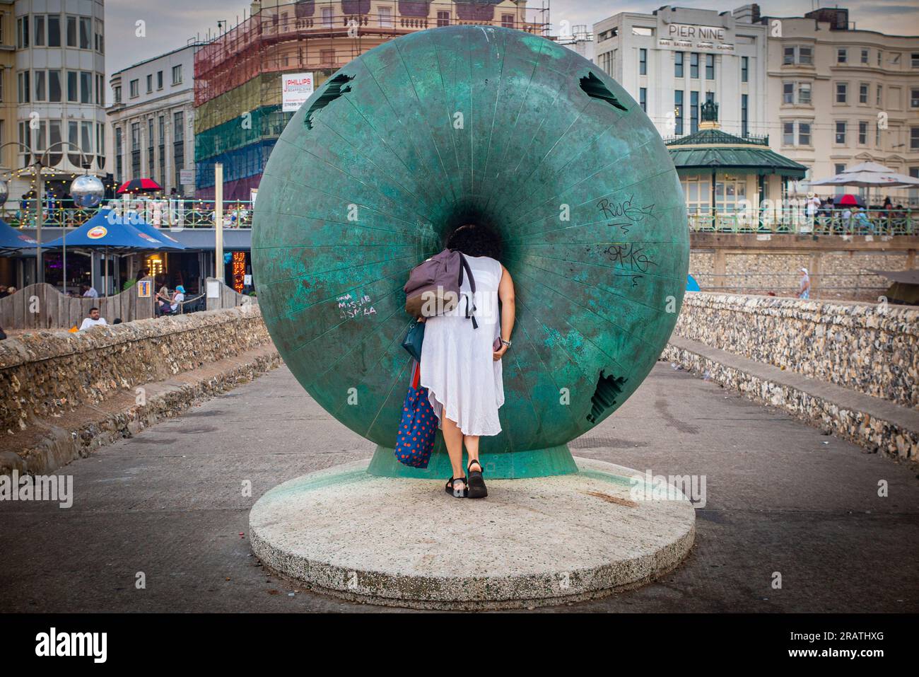 Eine Frau schaut durch die riesige Doughnut-Kunststatue an Brightons Uferpromenade Stockfoto