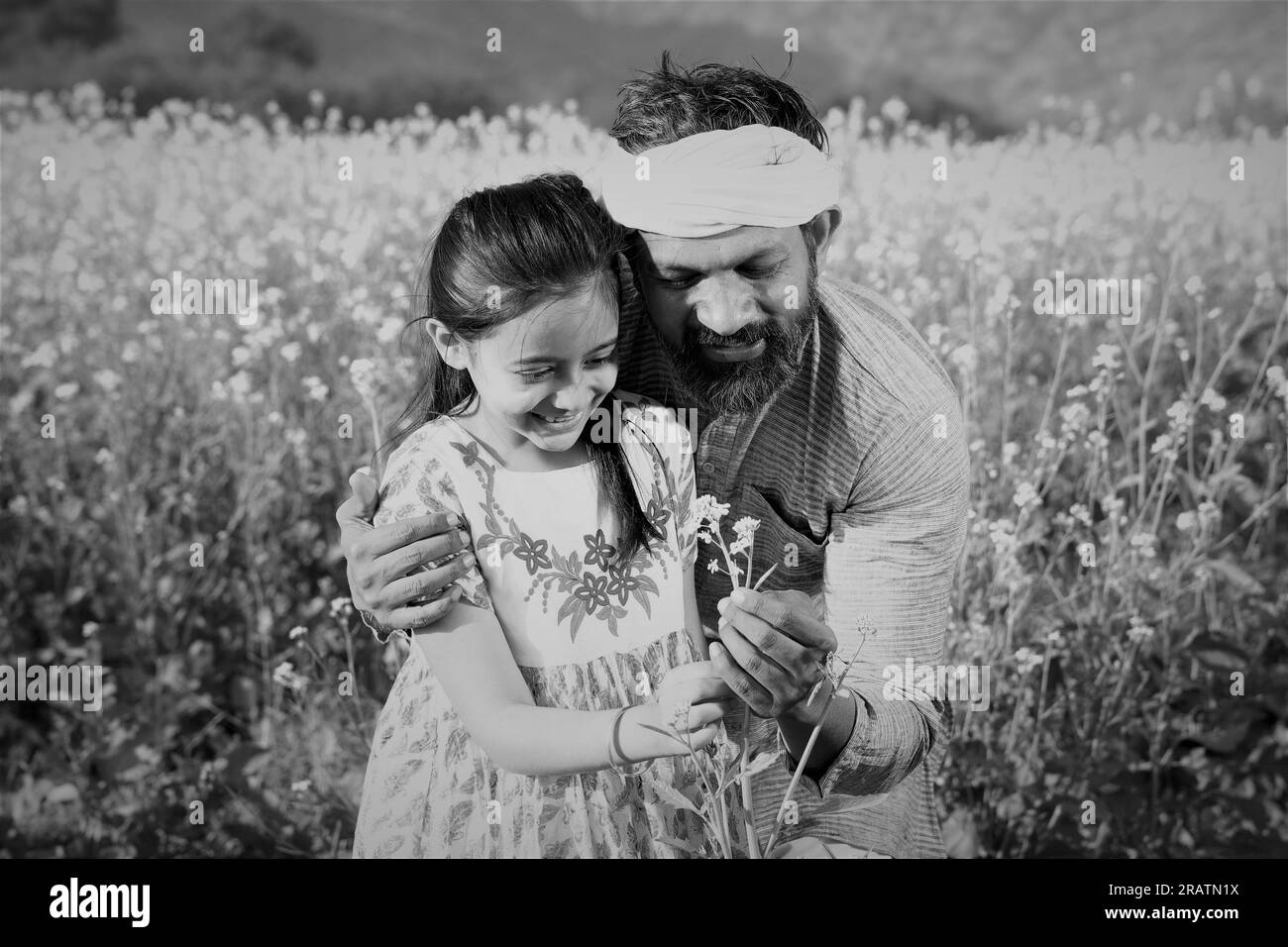 Vater und Tochter stehen auf einem Senffeld und genießen die blühenden landwirtschaftlichen Ernten. Vater unterrichtet seine Tochter über landwirtschaftliche Leistungen. Stockfoto