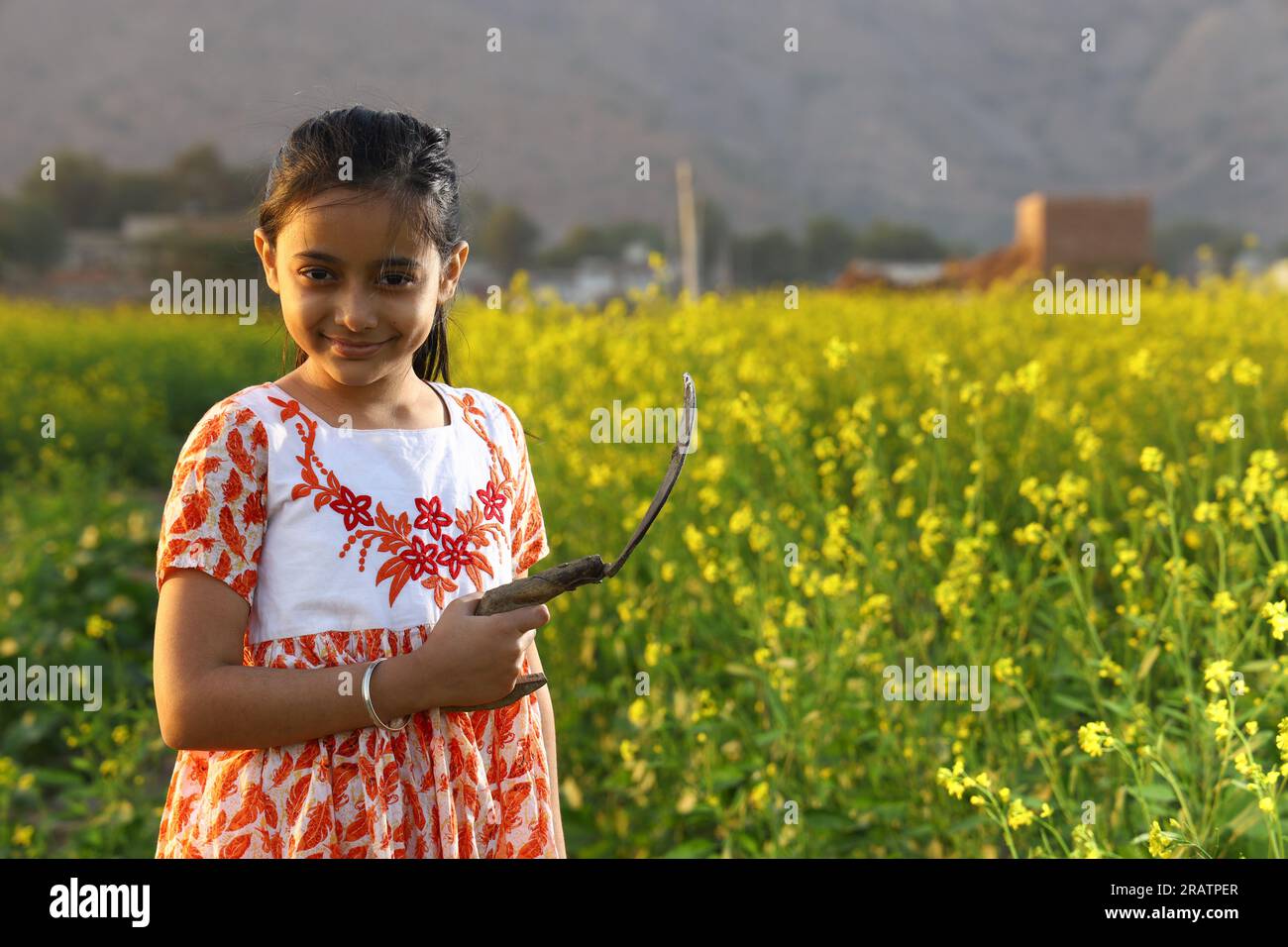 Ein indisches Bauernmädchen, das auf dem Senffeld steht und ein Kleid trägt. Ein Mädchen genießt die blühende Ernte mit Sichel in der Hand. Stockfoto