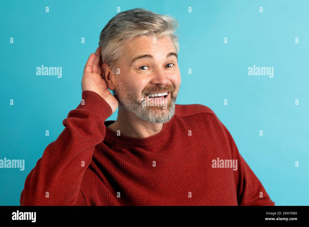 Mann mittleren Alters, lächelnd mit Hand über Ohr, blauer Hintergrund Stockfoto