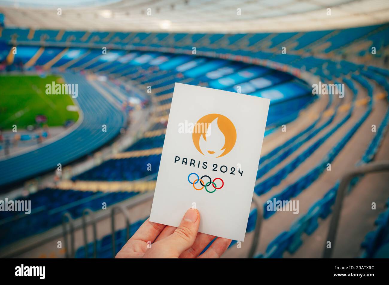 PARIS, FRANKREICH, 7. JULI 2023: Das Symbol annehmen: Athlet hält das berühmte Emblem der Olympischen Sommerspiele 2024 von Paris, mit modernem Stadion als Majestic Backdr Stockfoto