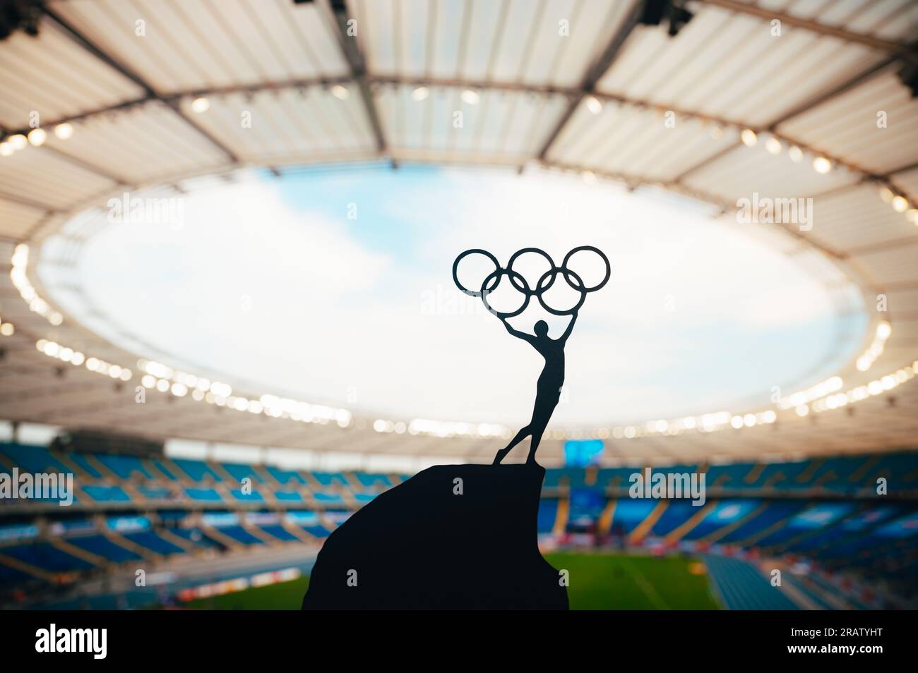 PARIS, FRANKREICH, 7. JULI 2023: Harmony of Athletics: Statue of Athlete umarmt den Olympischen Kreis gegen das moderne Olympiastadion. Ein Sportfoto für Paris 2 Stockfoto
