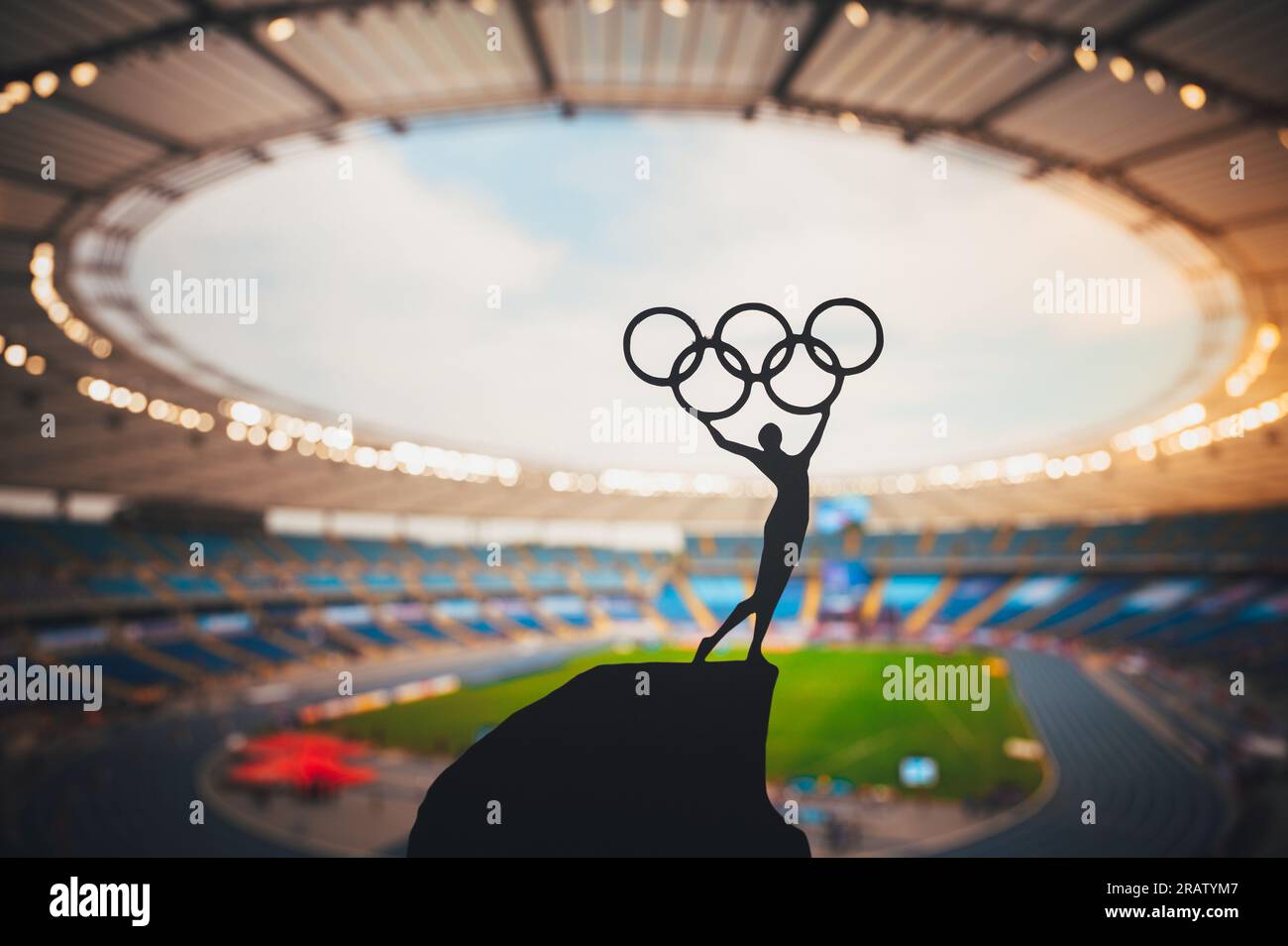 PARIS, FRANKREICH, 7. JULI 2023: Harmony of Athletics: Statue of Athlete umarmt den Olympischen Kreis gegen das moderne Olympiastadion. Ein Sportfoto für Paris 2 Stockfoto