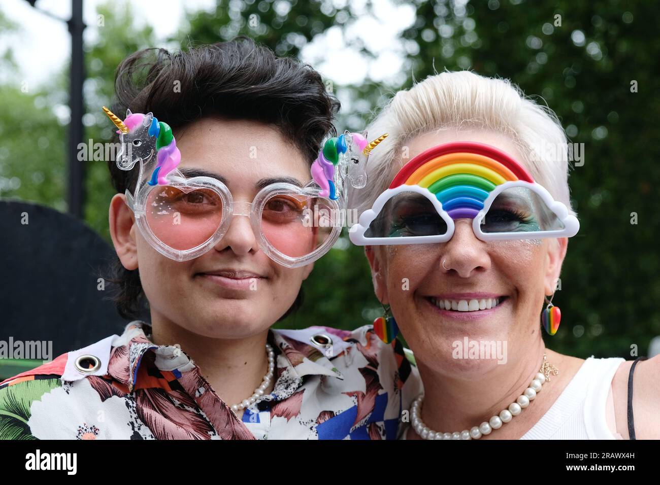 London, Großbritannien. Zwei Zuschauer, die die „Pride in London“-Parade beobachten, tragen eine neue Brille mit Regenbogen und Einhorn. Stockfoto