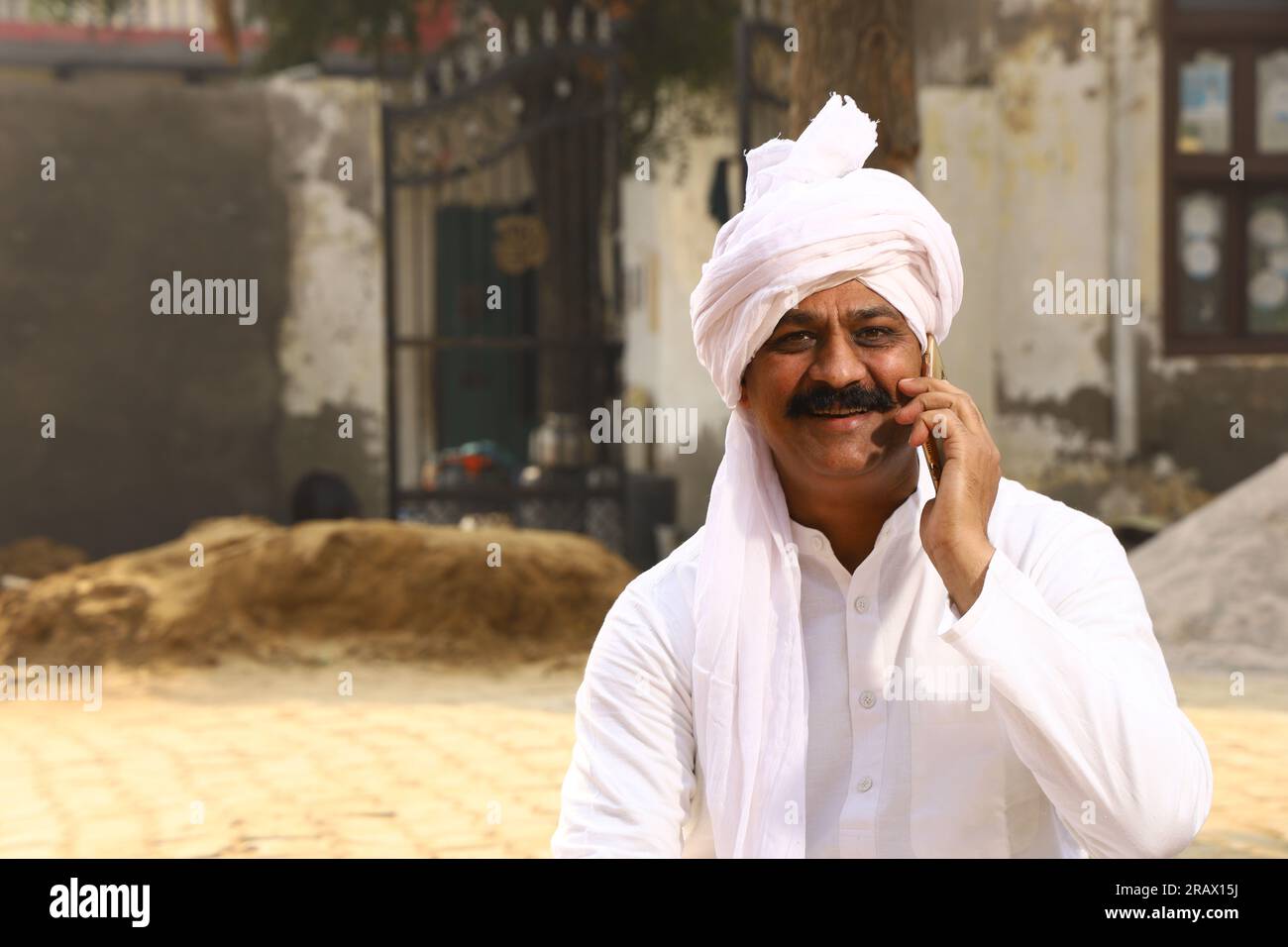 Mann sitzt auf dem Land und trägt Kurta-Pyjama, ein traditionelles Männerkleid für Männer in Nordindien am Tag und spricht gerne mit dem Handy Stockfoto