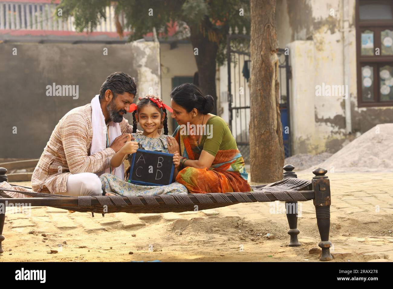 Glückliche ländliche indische Familie, die tagsüber vor ihrer Hütte zusammen saß, Tochter mit einem kleinen Whiteboard. Indien Lehren. Stockfoto