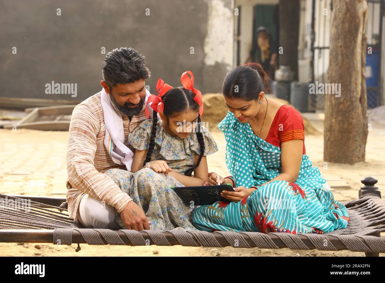 Glückliche ländliche indische Familie, die tagsüber vor ihrer Hütte zusammen saß, Tochter mit einem kleinen Whiteboard. Indien Lehren. Stockfoto