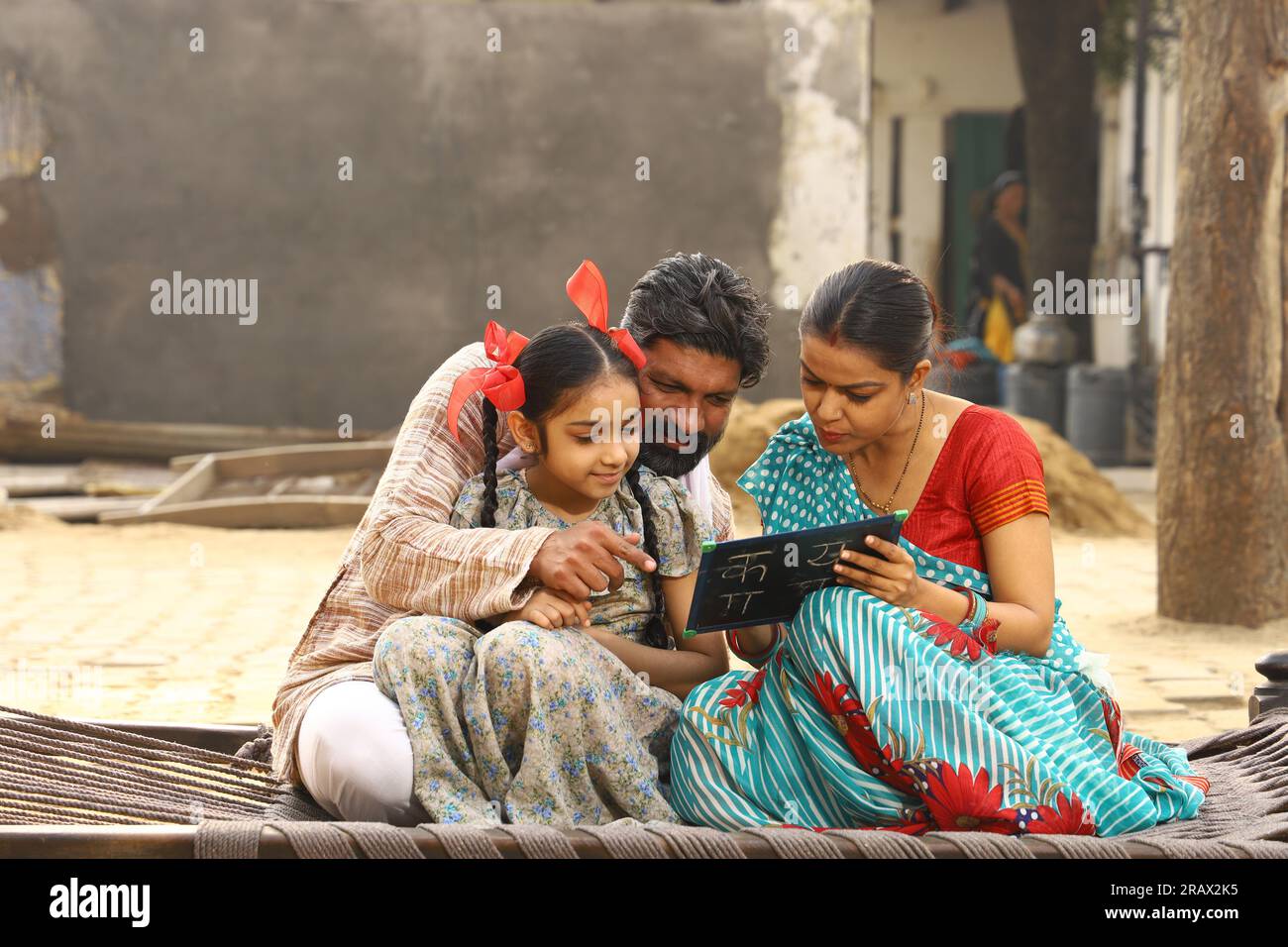 Glückliche ländliche indische Familie, die tagsüber vor ihrer Hütte zusammen saß, Tochter mit einem kleinen Whiteboard. Indien Lehren. Stockfoto