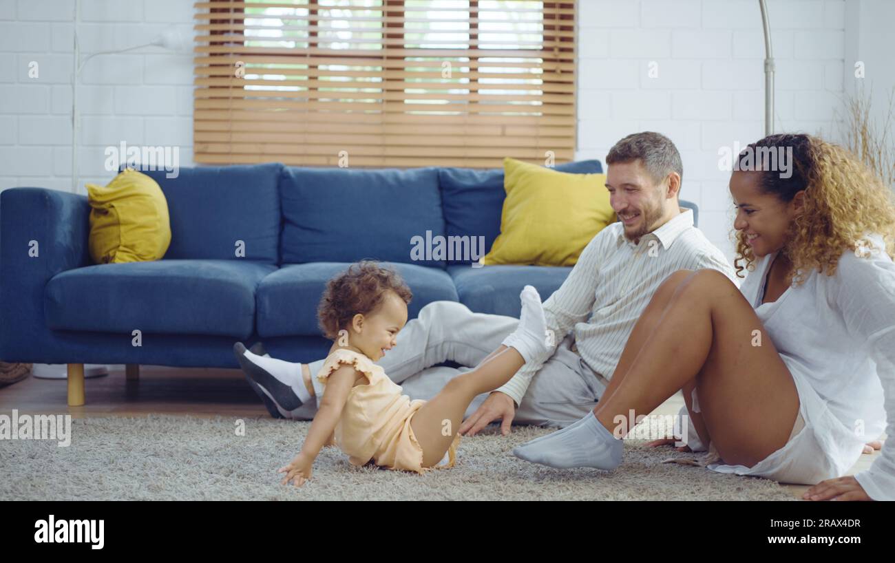 Eltern wärmen sich, indem sie ihre kleine Tochter umarmen und ärgern, während sie Zeit zusammen auf dem Boden im Wohnzimmer verbringen. Mom und Dad nutzen ihre Freizeit mit B Stockfoto