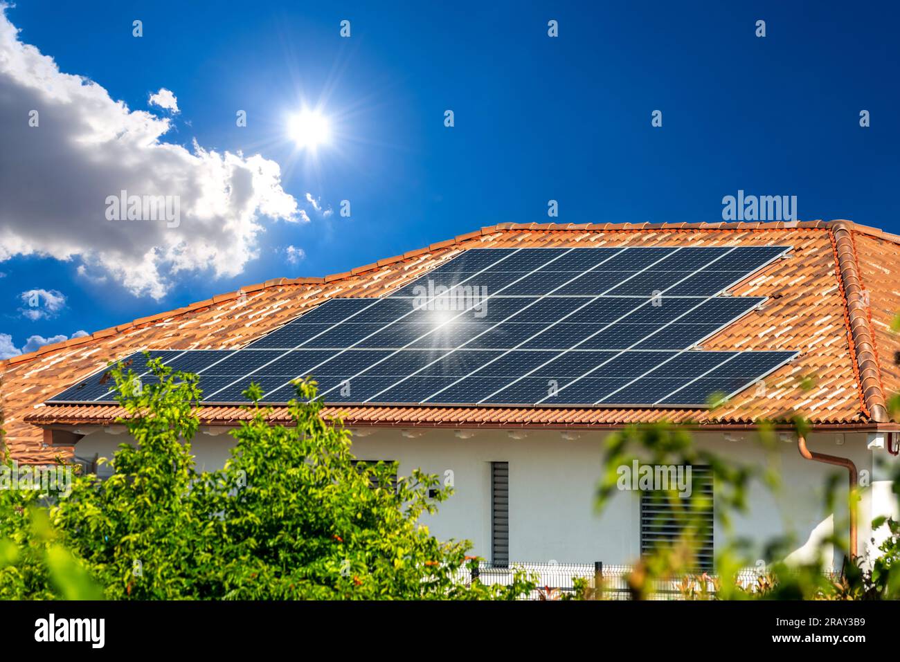 Sonnenkollektoren auf dem Fliesendach auf der Hütte am blauen Himmel mit Sonne und Sonnenreflexionen auf schwarzen Paneelen. Solarenergie Nachhaltige Ressourcen Stockfoto