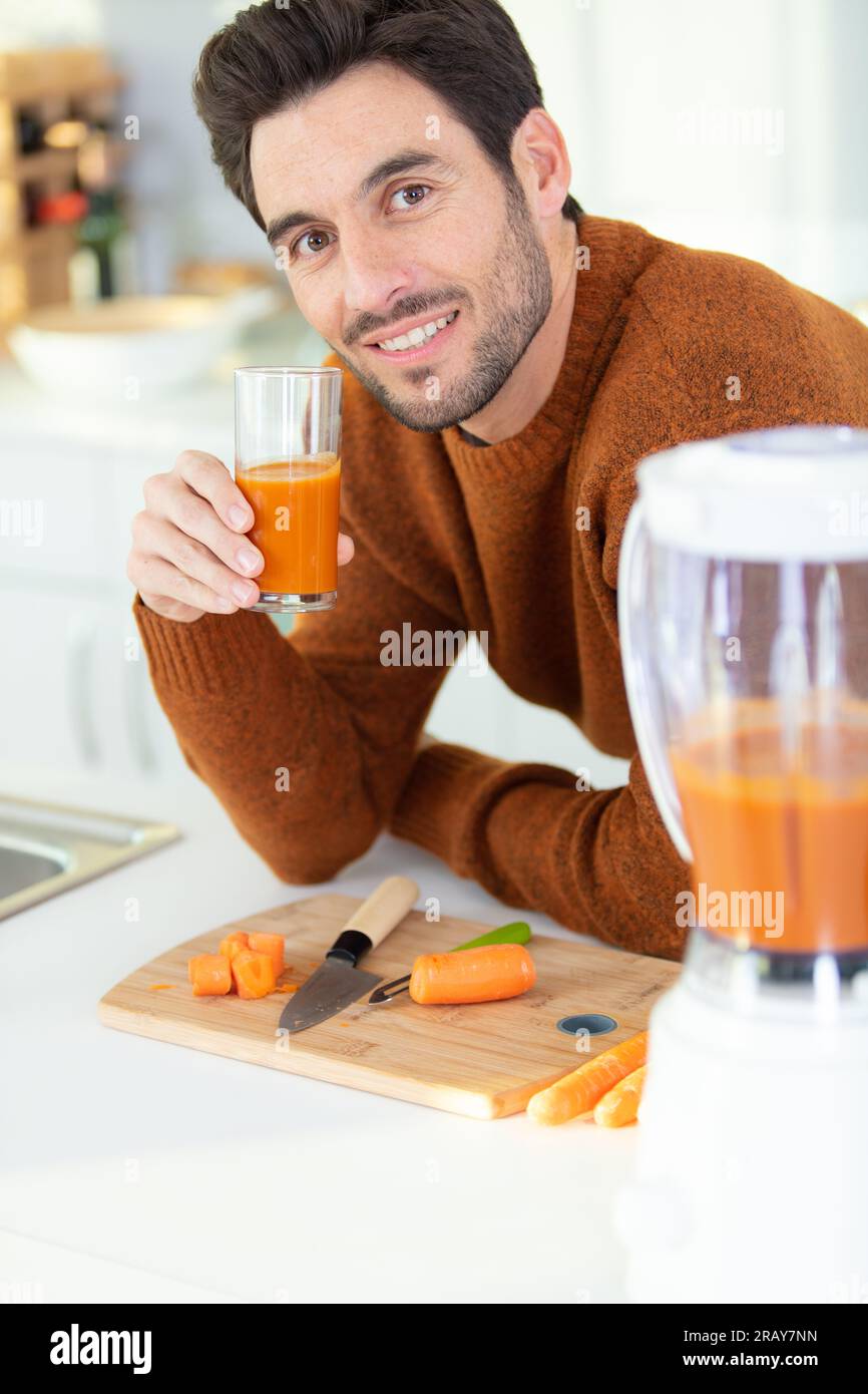 Junger bärtiger Mann trinkt frisch gepressten Karottensaft Stockfoto