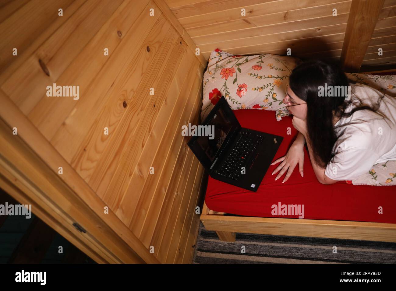 Erleben Sie das moderne Zeitalter der Online-Bildung, während eine junge, glückliche Frau im Bett mit ihrem Laptop arbeitet Stockfoto