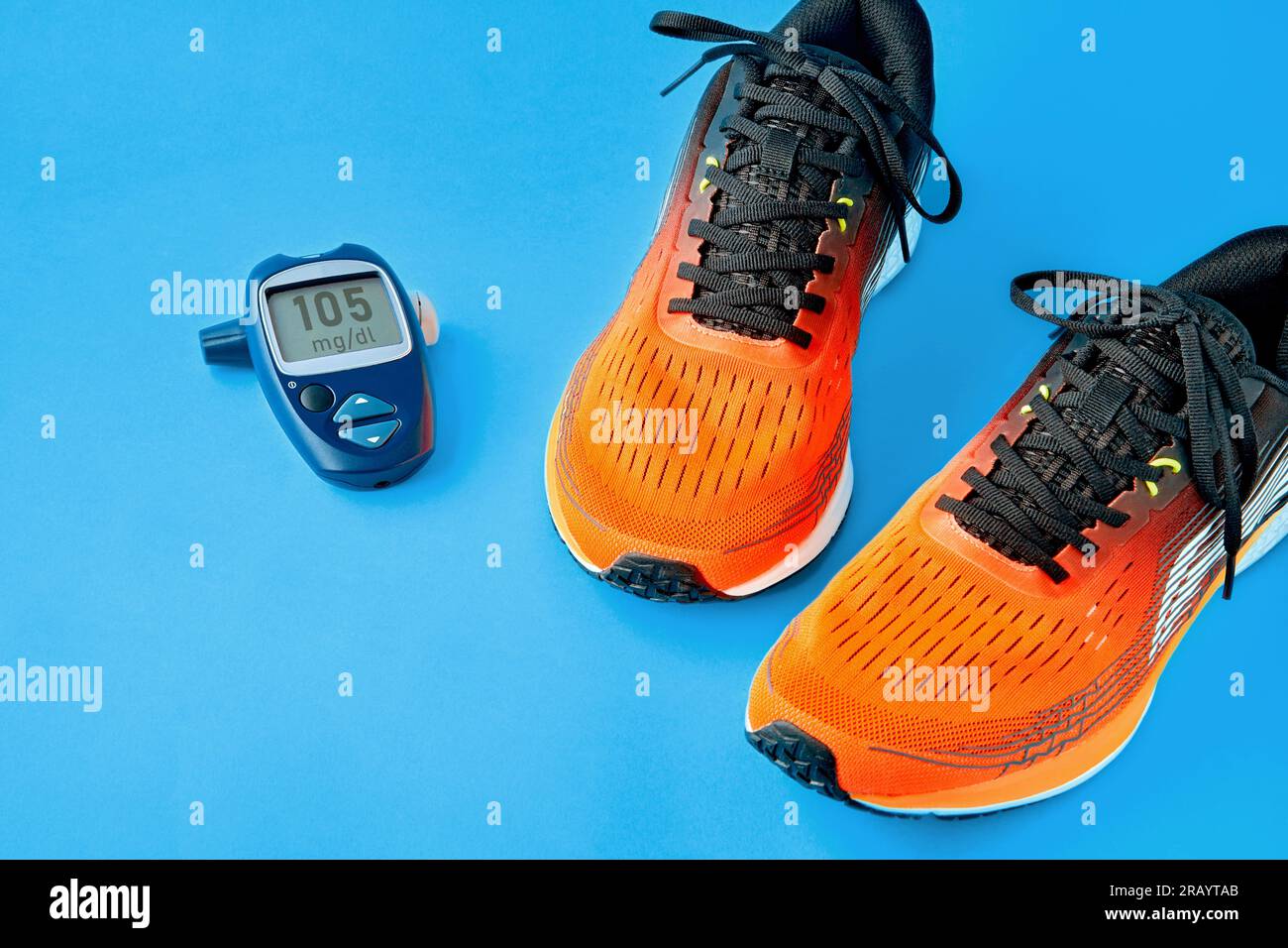 Orangefarbene Turnschuhe mit Glukometer zur Blutzuckermessung auf blauem Hintergrund. Lebensstil und Bewegung bei Diabetes Stockfoto
