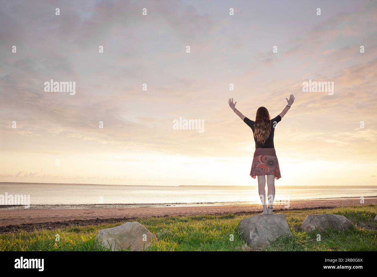 Eine Frau, die am Strand steht, mit ausgestreckten Armen Stockfoto