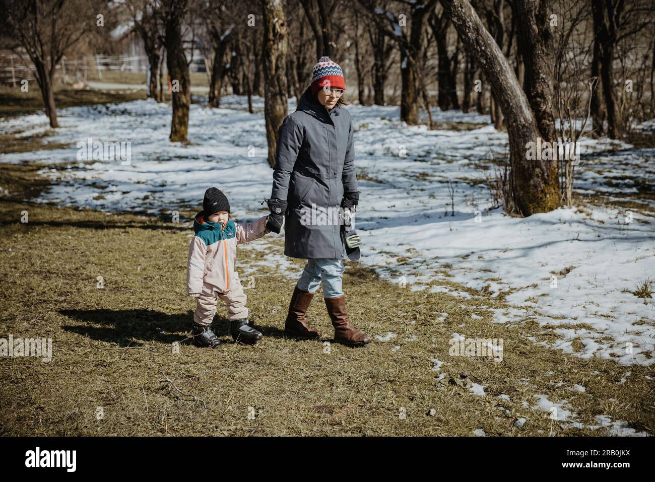 Mutter und Tochter gehen Hand in Hand über die verschneite Wiese Stockfoto