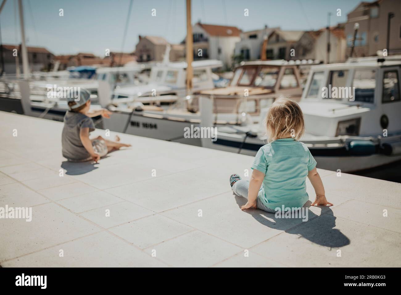 Bruder und Schwester sitzen auf der Promenade im Yachthafen, Insel Krk, Kroatien Stockfoto